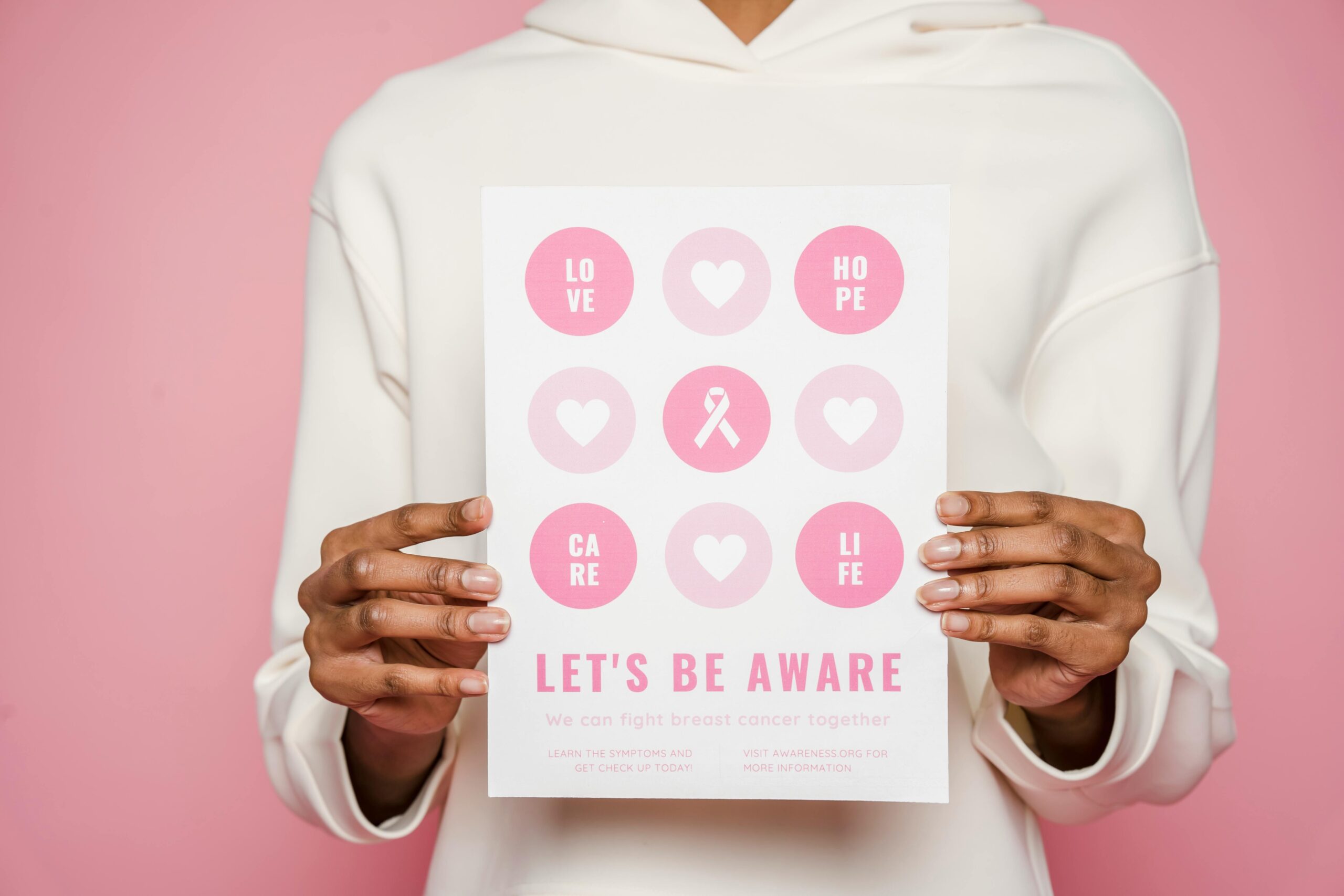 Person holding a breast cancer awareness poster with pink icons and messages of love, hope, care, and life.